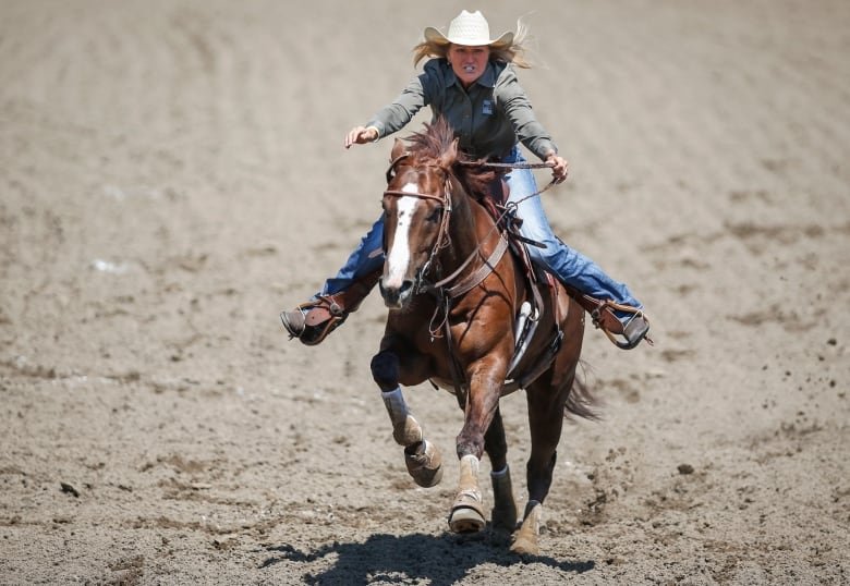 A woman in a white cowboy hat rides a horse with a blaze.