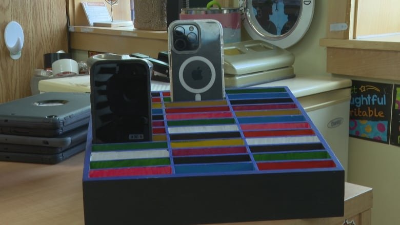 Two cellphones rest in slots of a colourful caddy, sitting on the desk of a junior high school classroom in Corner Brook, Nfld.