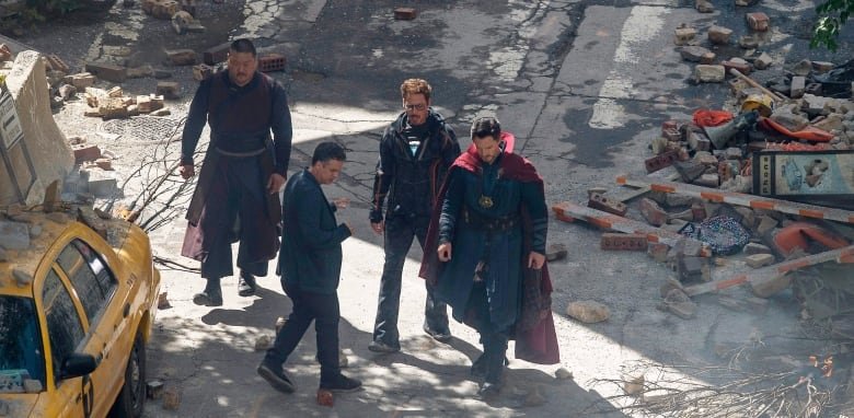 Four people stand in a ruined street, they are seen from above.