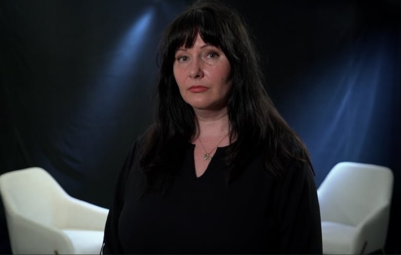 A woman is seen standing in front of two chairs.