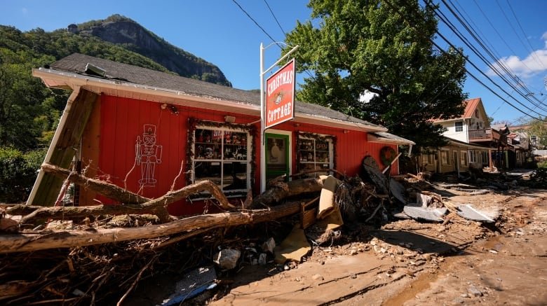 A red building with rubble and fallen tree branches in front of it is visible. Farther down the road, more rubble is visible.