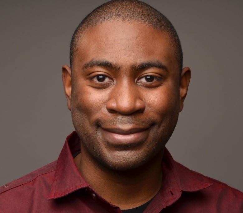 A portait of a smiling man wearing a burgundy dress shirt.