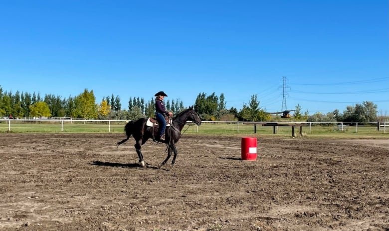 A woman with a cowboy hat rides a horse in an outdoor arena.