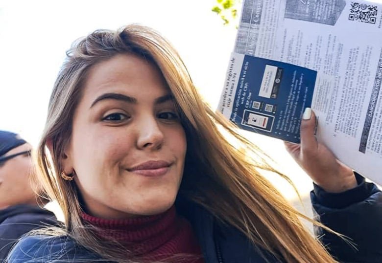 A smiling woman with long hair holds up a document for a selfie.