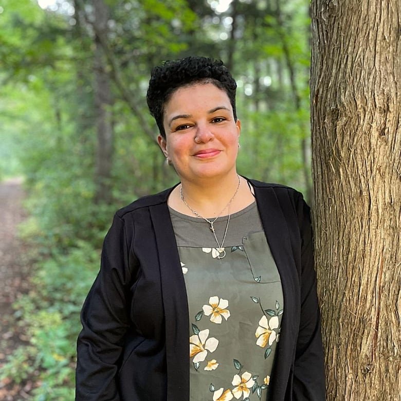 portrait of woman with short brown hair leaning against a tree in a forrest.