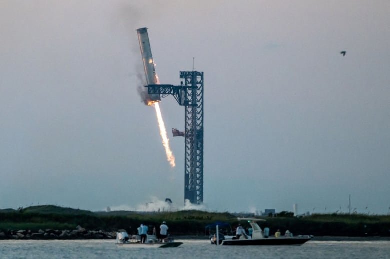 A booster rocket is grabbed by metal arms at the launch pad.