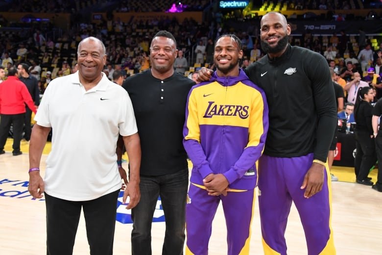 Four men stand in a row on a basketball court and pose together for a photograph.