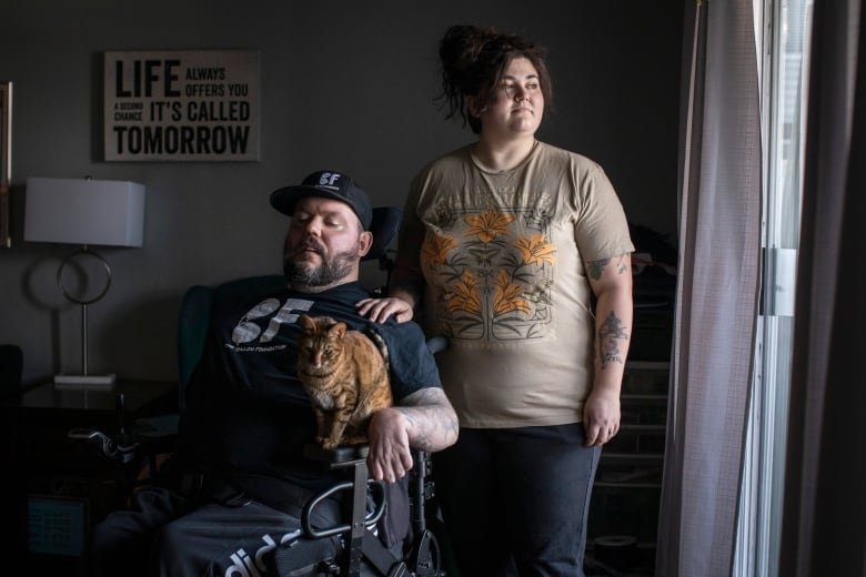 A man in a wheelchair, holding a cat, and a woman pose for a picture.