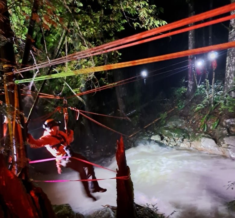 A person is seen using a highline to traverse a river at night.