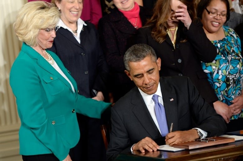 An image of Lilly Ledbetter watching as President Barack Obama signs executive actions, with pending Senate legislation, aimed at closing a compensation gender gap that favors men.