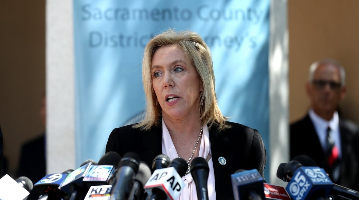 A woman stands at a podium answering questions.