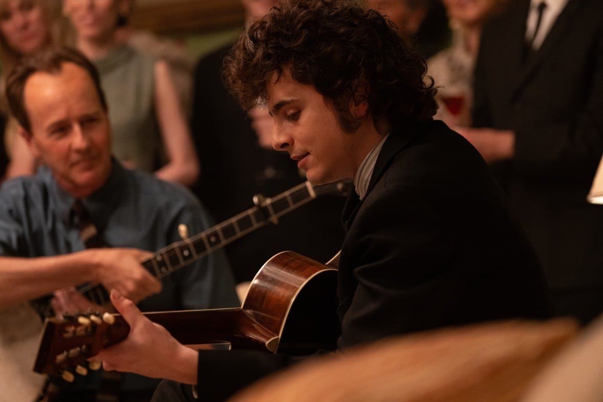 A man plays guitar. To his left is a man holding a banjo.