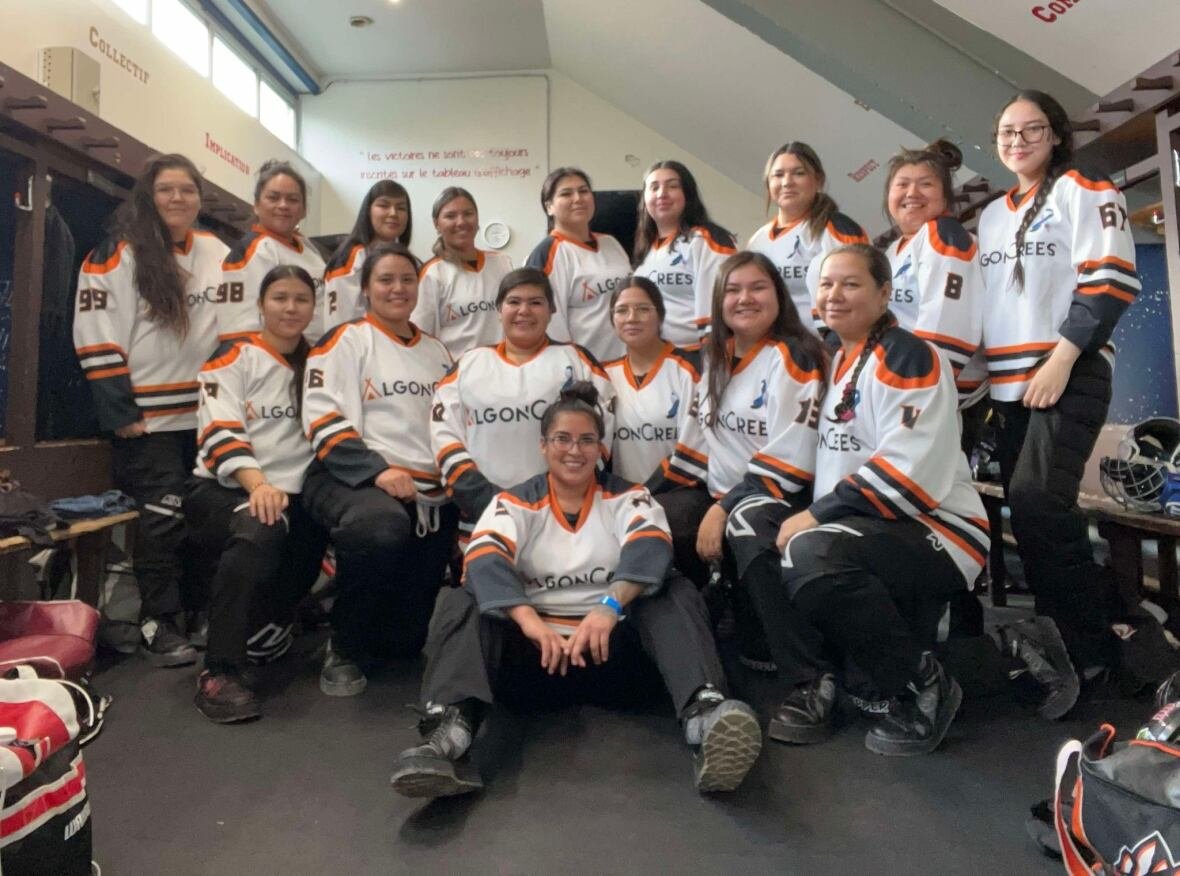 A group photo of women in their white, orange, and black broomball jerseys.