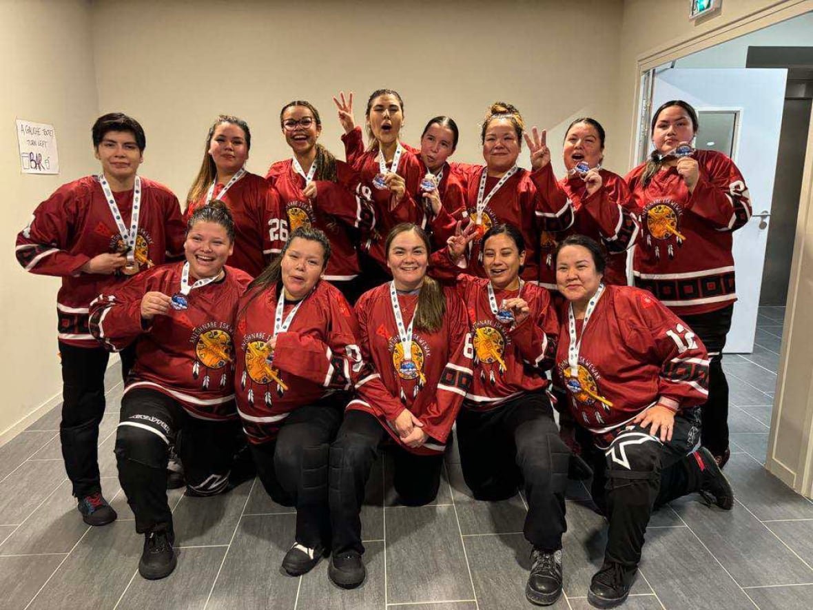 Anishinaabe Iskwewak pose with their bronze medals. Their jerseys are maroon, black, orange and white.