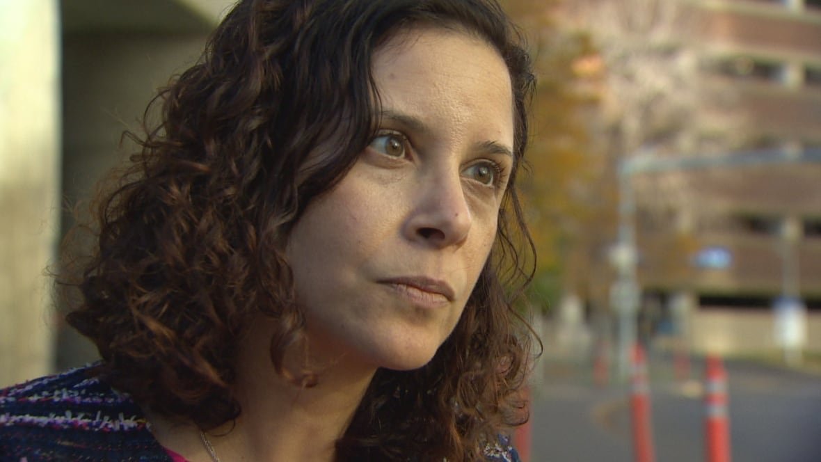 A woman with curly brown hair stands by the side of the street.