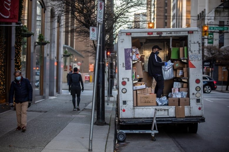 A man in the back of a package truck lifts boxes.