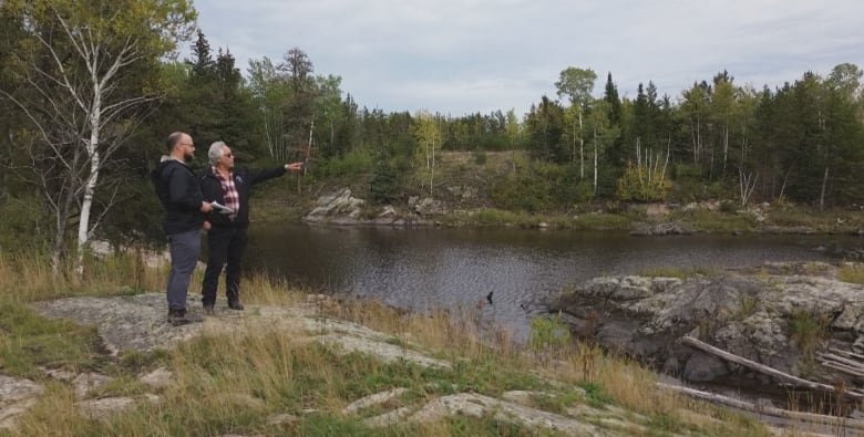 A man and a reporter stand on a granite outcrop on a wilderness river.