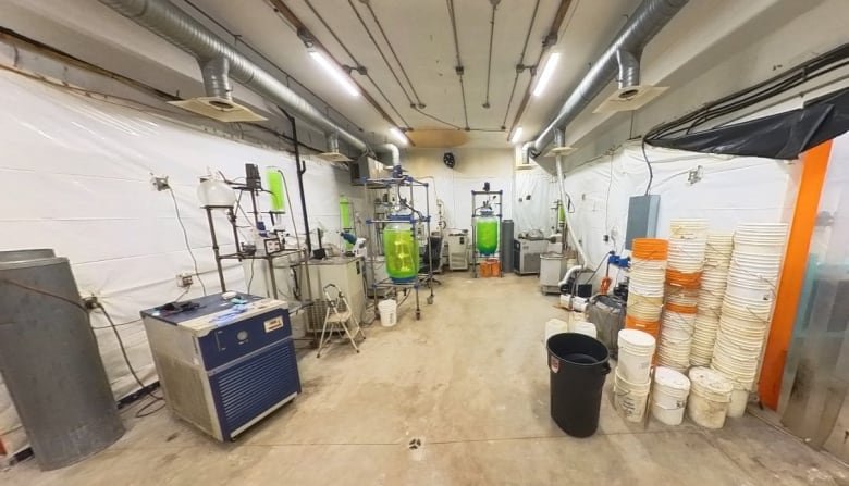 The interior of what looks like a lab with various containers and machines on a wooden floor under large hood vents and fluorescent lights.