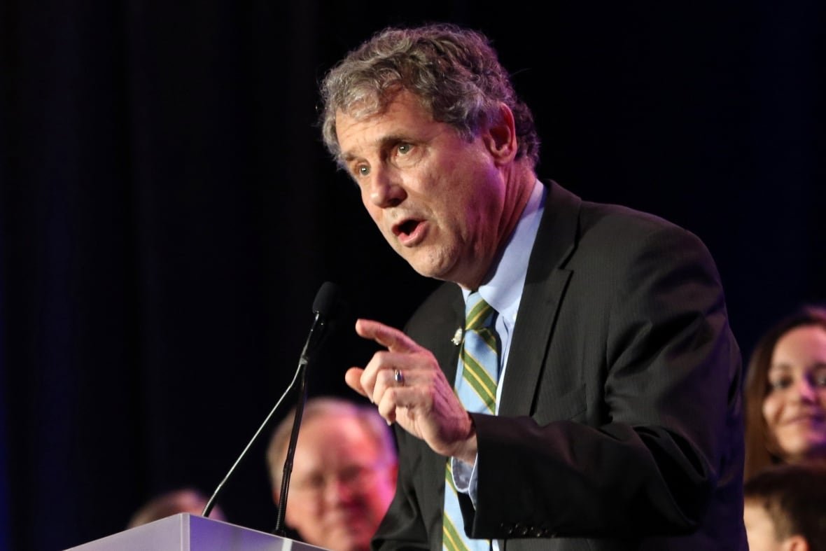 A man in a suit speaks at a microphone.