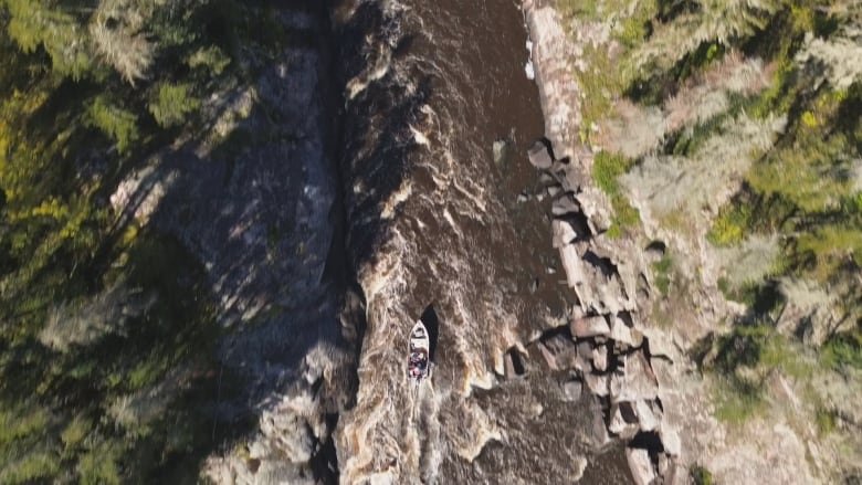 A motorboat is pictured in an aerial photo running a set of rapids on a river.