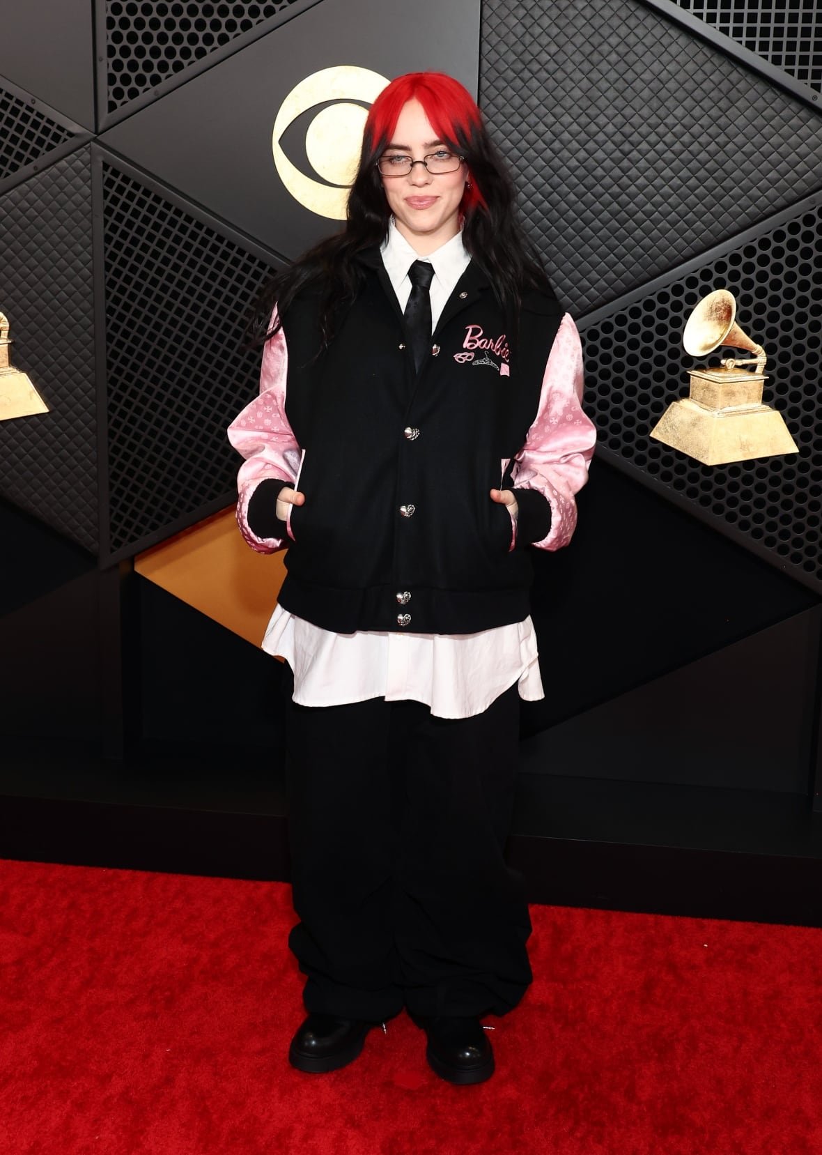 A woman with red and black hair wears a letterman jacket customized with the Barbie logo.