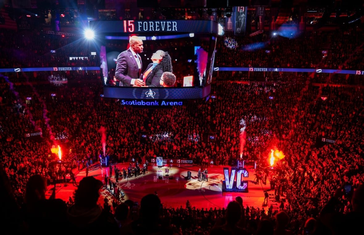 A packed stadium watches on as a large screen over a basketball court shows people embracing.