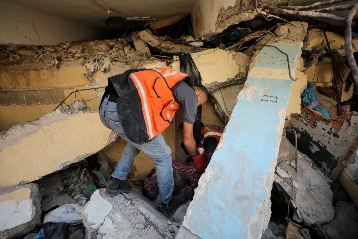 A man in an orange vest looks through rubble