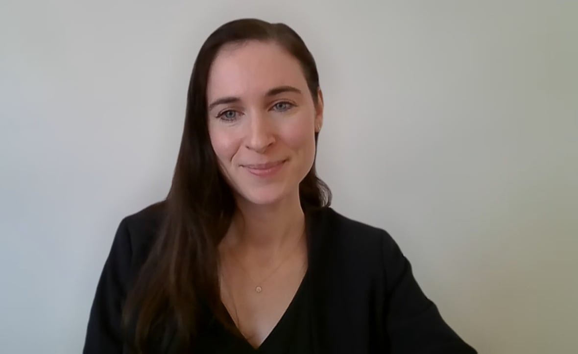 A woman sits in front of a white wall during a video call.