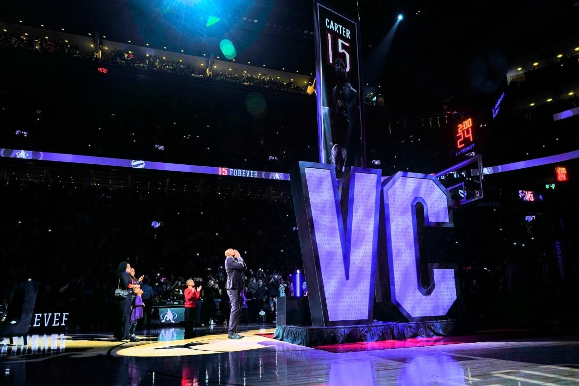 People on a basketball court look up as a banner is lifted to the rafters.