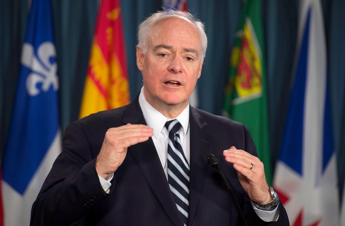 A man with thin white hair wearing a blue suit and tie.