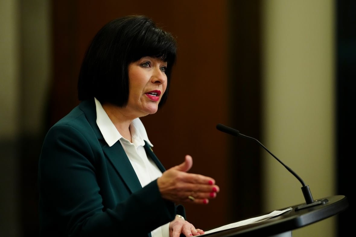 A woman in a green suit speaks at a podium.