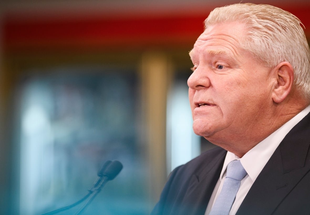 Close-up of a man's face in the middle of talking, shown in profile view in front of a blurred background.