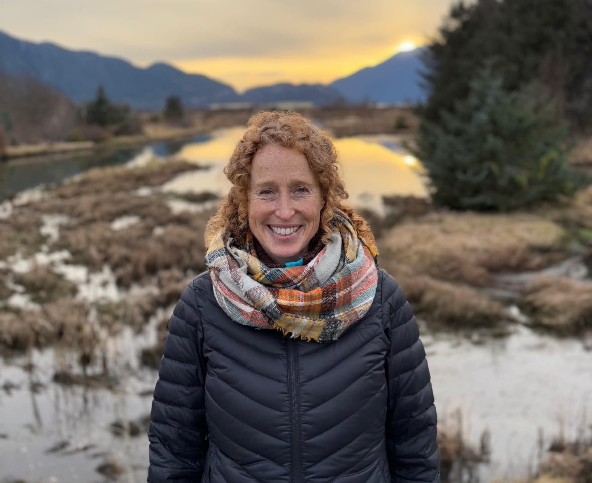 A woman with red curly hair in front of a winter landscape.