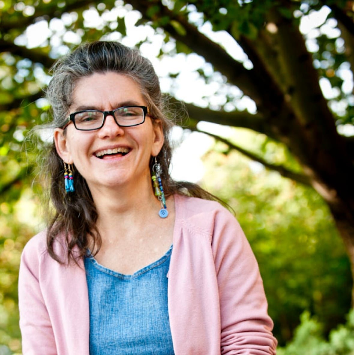 A woman wearing a pink sweater and blue shirt is smiling at the camera.