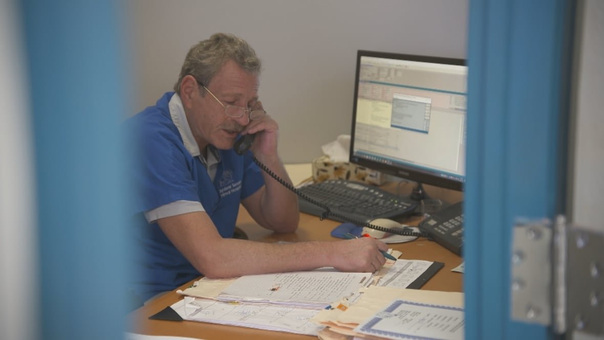 Veterinarian Howard Covant, seen through a door, sits in his office, speaking into a telephone