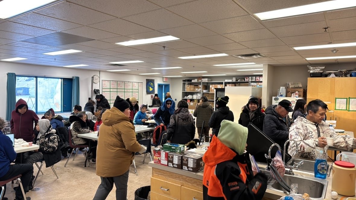 People in coats sit and eat in a classroom