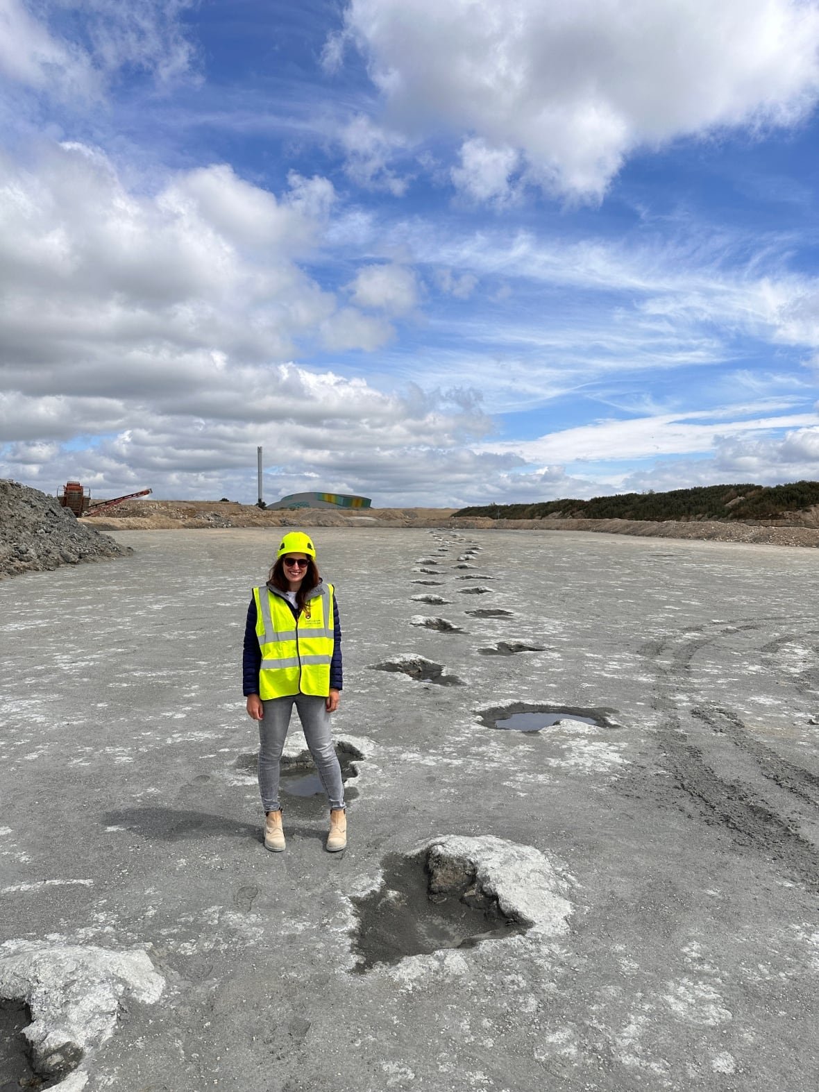 Woman in helmet and high-vis vest beside a dinosaur trackway