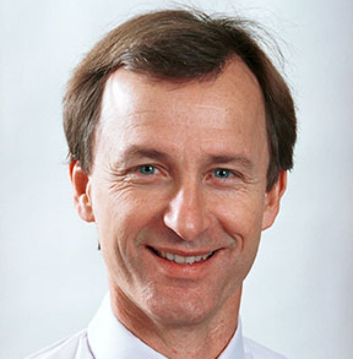 A man in a shirt and tie smiles at the camera.