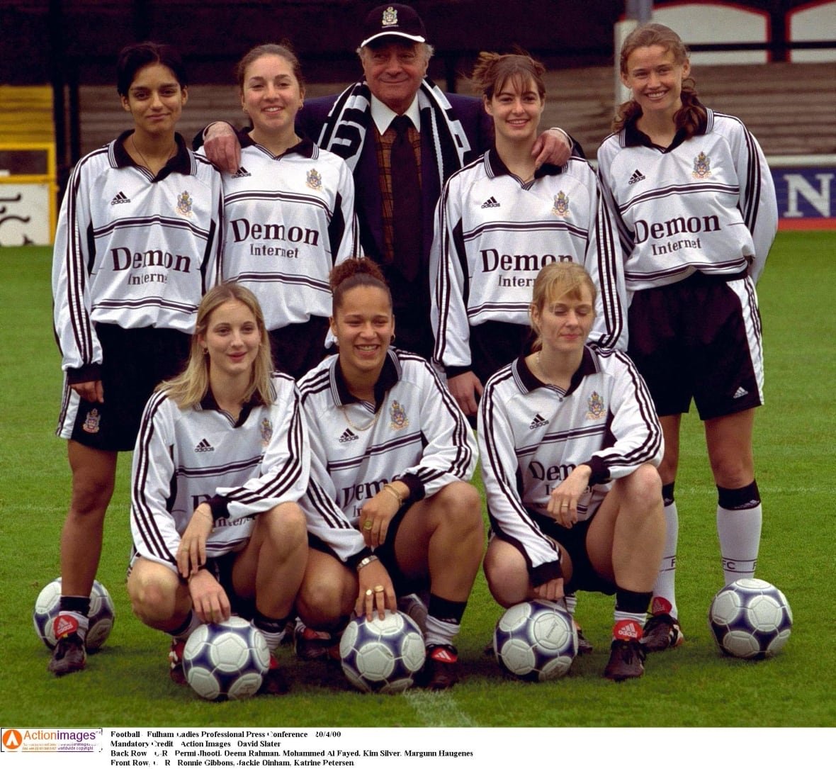 Players on a women's soccer team pose with a man in a tie and ballcap.