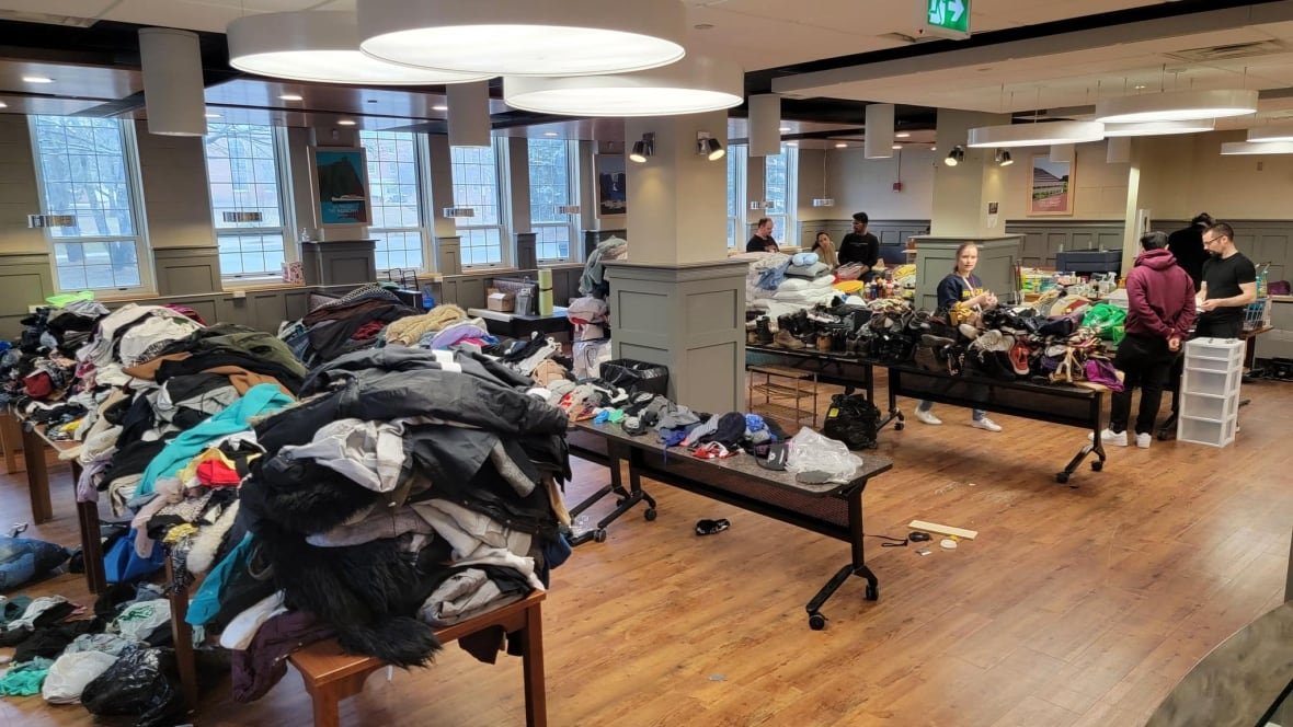 Tables full of clothes in a large room with wooden flooring.