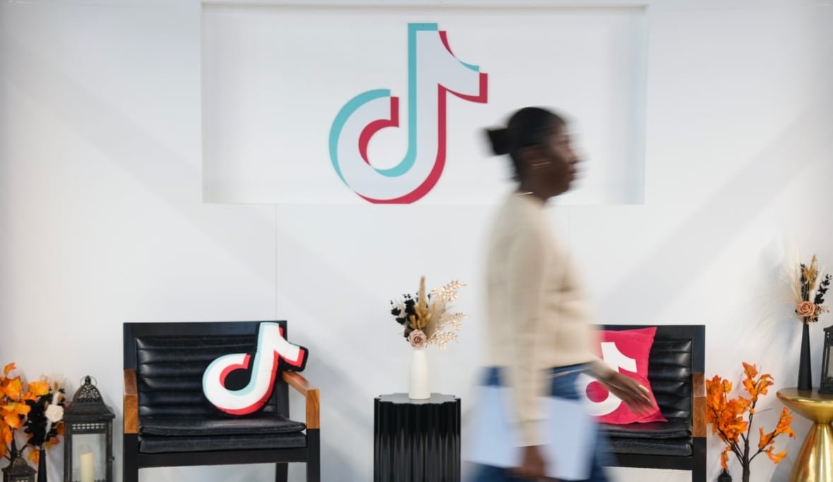 A woman walks by chairs in an office, with the TikTok logo in the background.