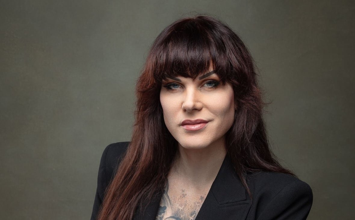 A woman in a blazer with tattoos poses for a portrait.