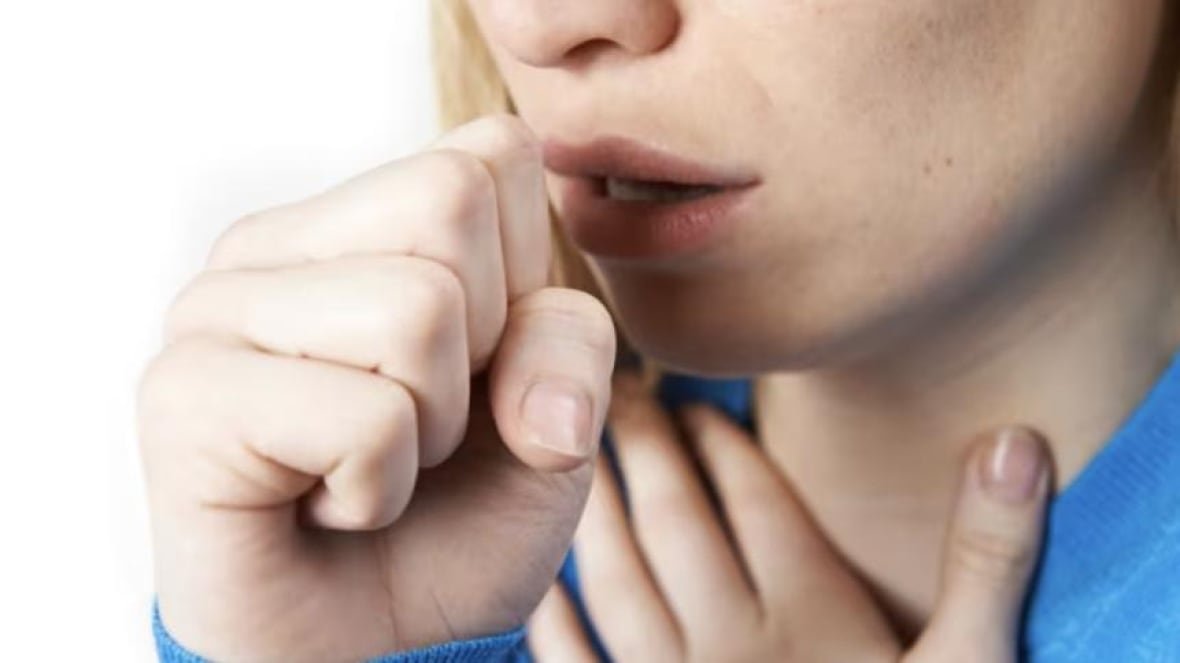 A girl holds her throat as she coughs into her other hand.