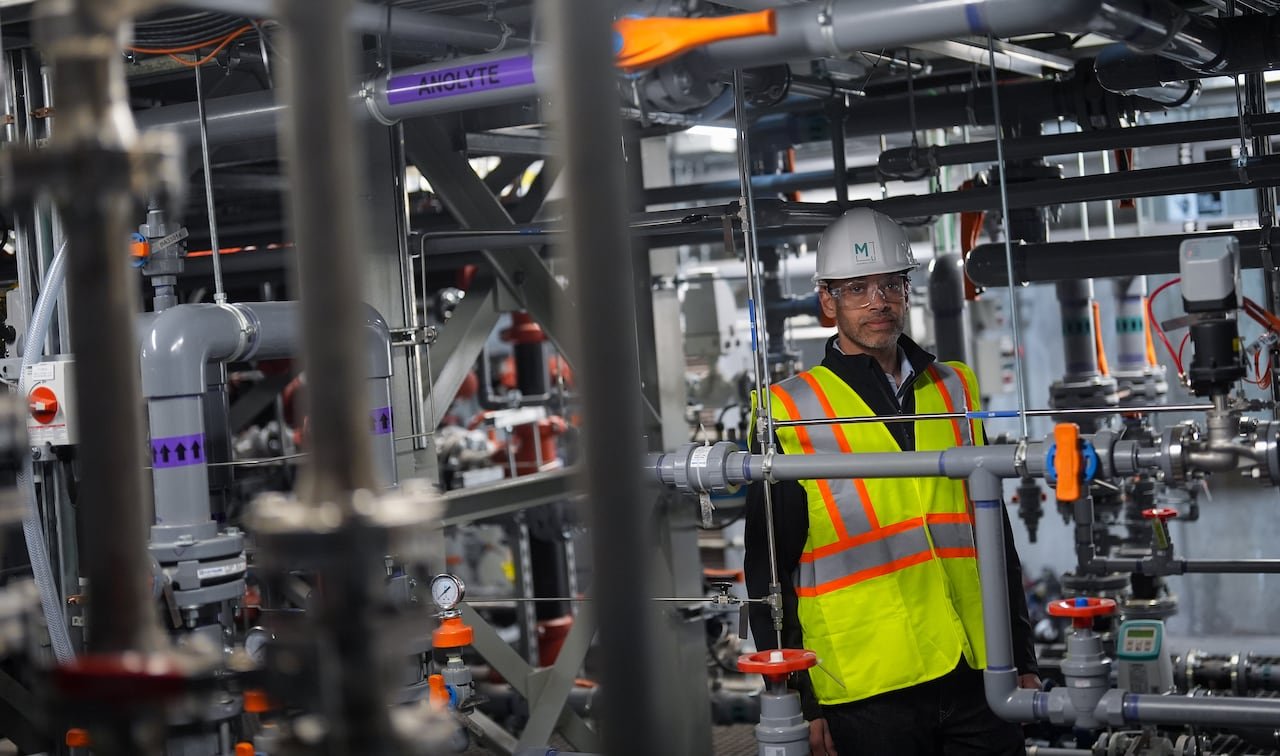 A man in a high-vis vest is seen among industrial equipment.