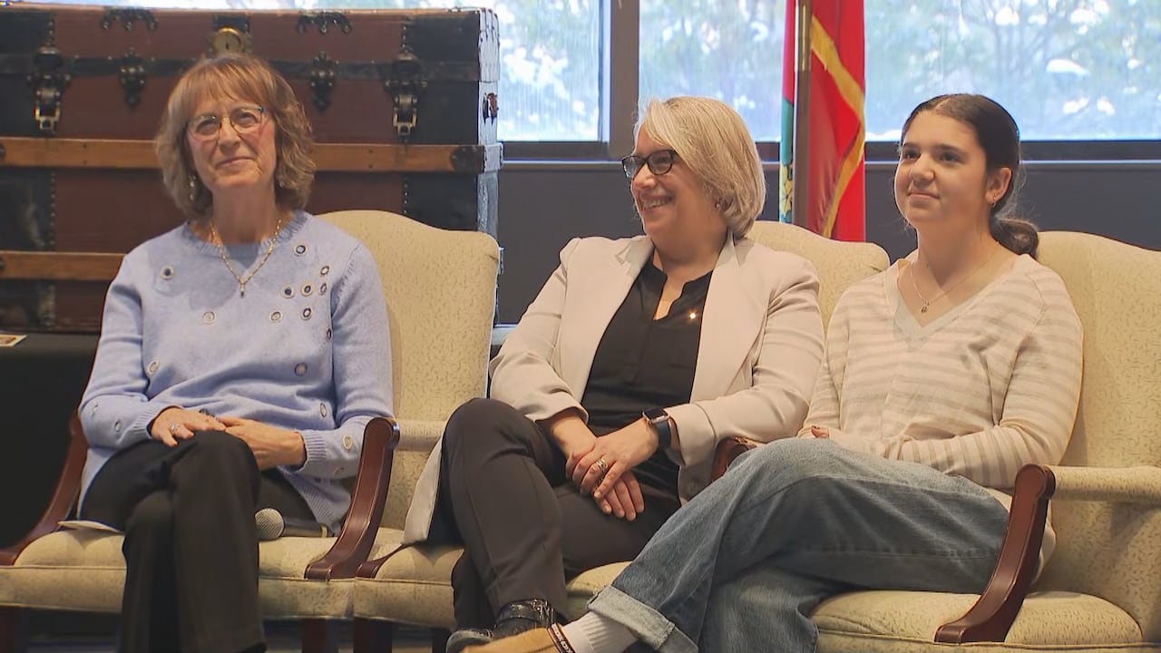 Two smiling women and a smiling teen girl sit in an indoor room.